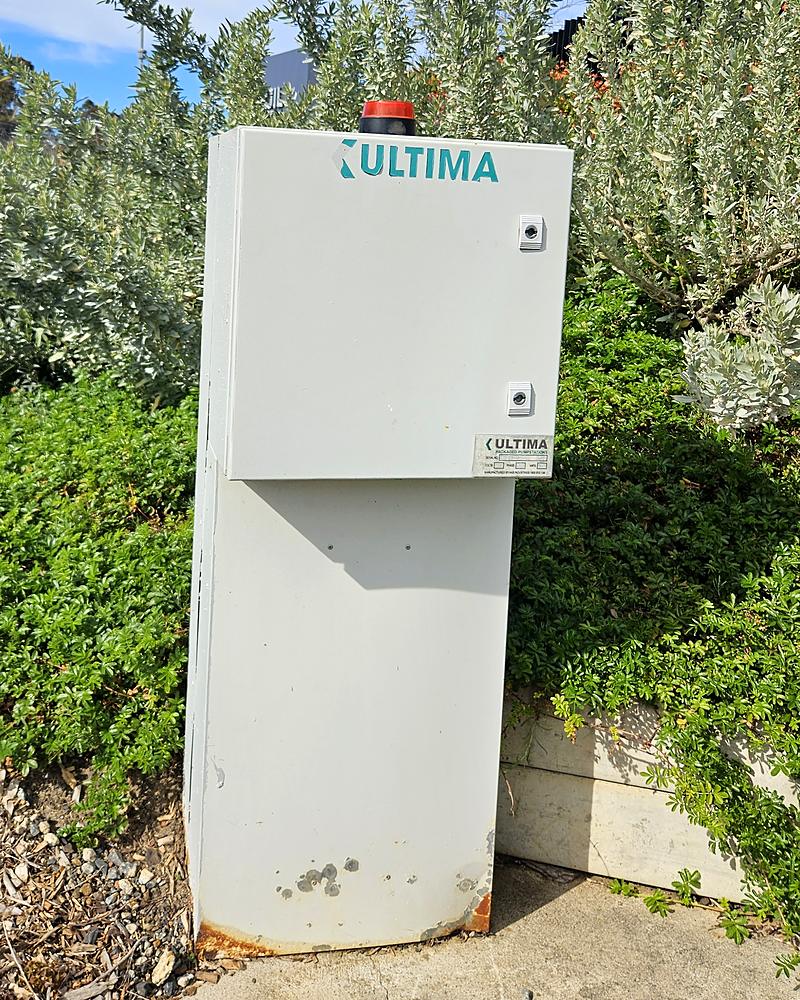 Outdoor wastewater pump station control panel with a high level alarm strobe on top, standing unattended in an empty landscaped yard